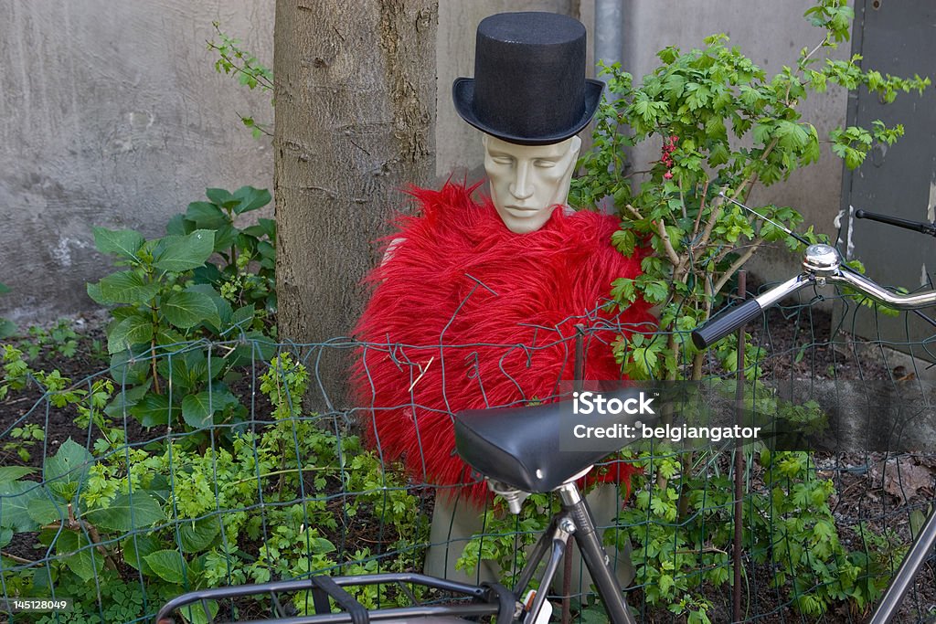 Parked bicycle and mannequin outside house in Dordrecht A strange scene outside a house in Dordrecht in the Netherlands. A bicycle is parked outside the door, and there is a mannequin dressed in a tall hat and red clothing. Bicycle Stock Photo