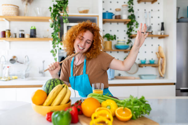 istock Funny beautiful woman singing into spatula, cooking in modern kitchen, holding spatula as microphone, dancing, listening to music, playful girl having fun with kitchenware, preparing food. 1451282010