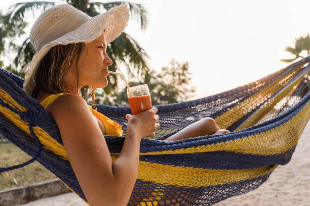 istock Smiling woman drinking smoothie in a hammock on the beach. 1451285361