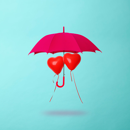 Heart-shaped balloons shared pink umbrella floating in mid-air against light blue background.