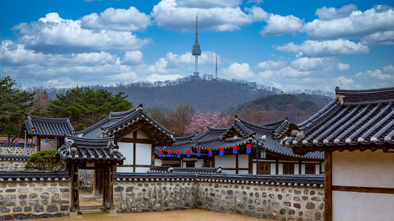 The iconic spire of Namsan Tower overlooking tourists visiting the traditional wooden homes of Bukchon Hanok village in Seoul, South Korea’s vibrant capital city.