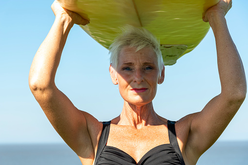 Cropped shot of a senior woman holding up a surfboard on her way to go surfing