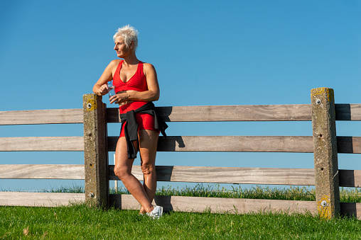 Senior Woman resting after Jogging in nature. The Netherlands. Low angle view. Medium shot.