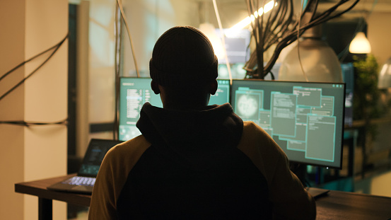 Silhouette of male hacker breaking firewall encryption to plant trojan virus, looking to steal valuable data late at night. Young thief using computer malware to hack online web system.