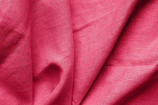 Textured folds of linen fabric in red, magenta color. Textile background, top view, copy space