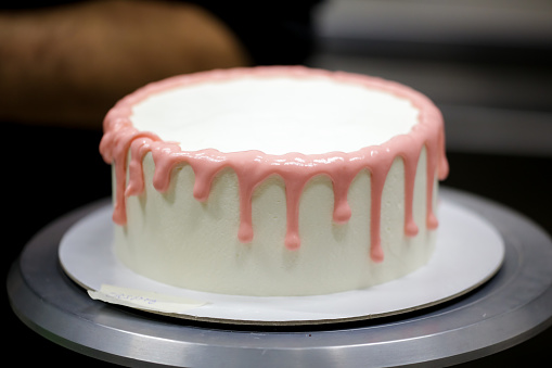 cake chef designer preparing a pink dripping on white frosted cake for baby girl birthday celebration at kitchen lab