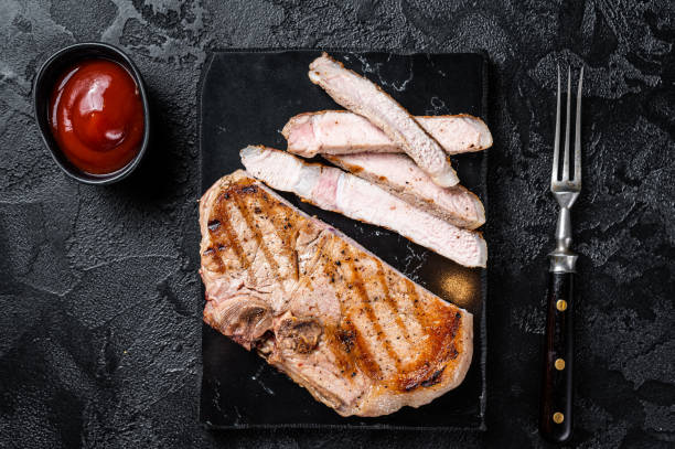 istock Grilled slised pork Chop or T-bone meat steak. Black background. Top view 1451308803