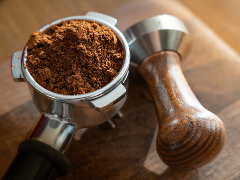Fresh ground coffee in portafilter with wooden tamper in close-up