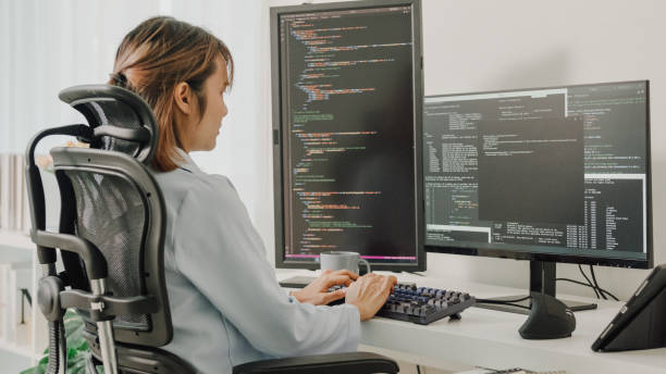 las jóvenes desarrolladoras de software asiáticas que usan la computadora para escribir código sentadas en el escritorio con múltiples pantallas trabajan de forma remota en casa. - java fotografías e imágenes de stock