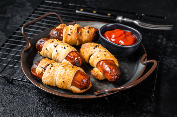 istock Pigs in Blanket puff pastry sausage wrap roll. Black background. Top view 1451310452