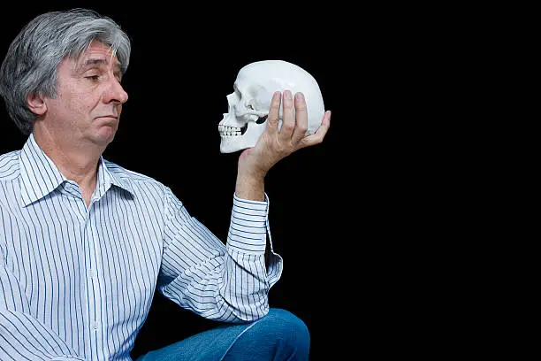 Gray haired man staring at a skull