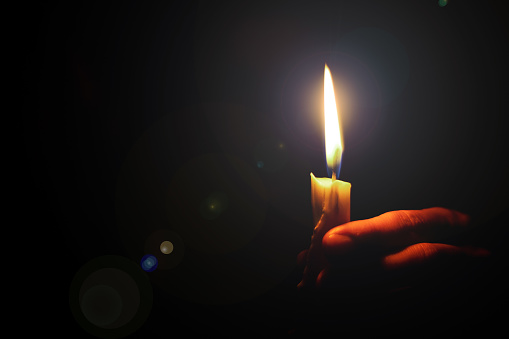 glare from a candle flame illuminates a woman's hand in a dark room, religion