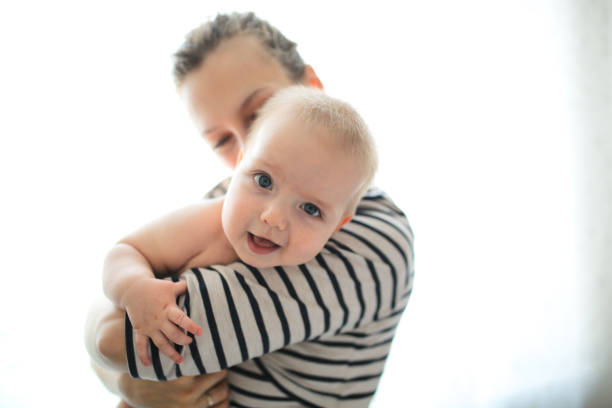 funny baby 6 months mom in her arms against window funny baby 6 months mom in her arms against the window. Mom tickles and gently kisses the baby. Concept maternal love and motherhood, soft focus, toning and lifestyle half dozen babies stock pictures, royalty-free photos & images