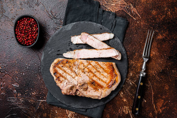 istock Roast BBQ pork Chop or T-bone meat steak sliced on a board. Dark background. Top view 1451313761
