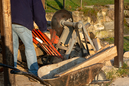 Sawing firewood with circular saw. Man cutting fuelwood on a large circular saw blade. Preparing firewood for the winter season.