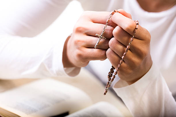 Person praying with Jesus cross in hand Woman praying, holding rosary beads over prayer book, close-up, mid-section. Vertical version can be found in my portfolio. rosary beads stock pictures, royalty-free photos & images