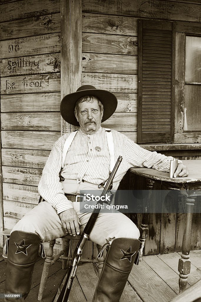 Weary Alter Cowboy-Sheriff Sitzbereich mit Gewehr auf verwitterten Veranda - Lizenzfrei Cowboy Stock-Foto