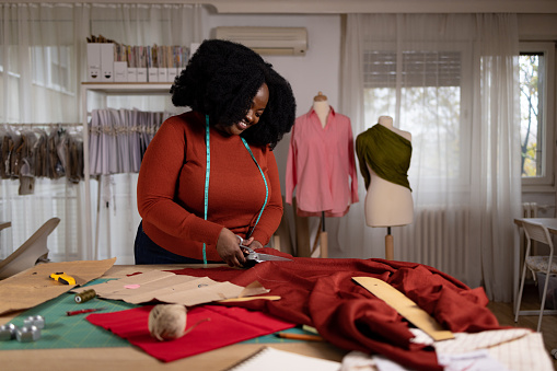 Happy African American female designer cutting textile while working in a design studio.