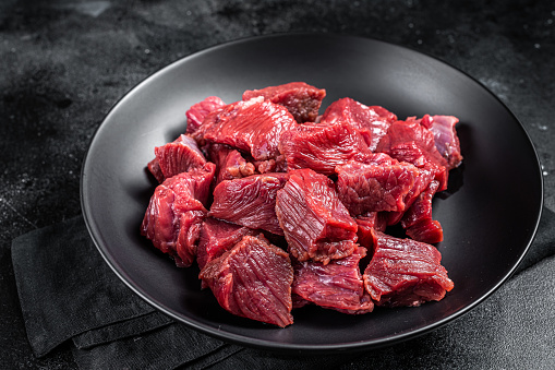 Raw Diced game meat of wild venison dear. Black background. Top view.