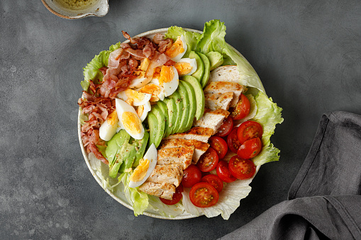 Cobb salad with bacon, avocado, tomato, grilled chicken, eggs on dark background. American salad. Healthy food. Top view.