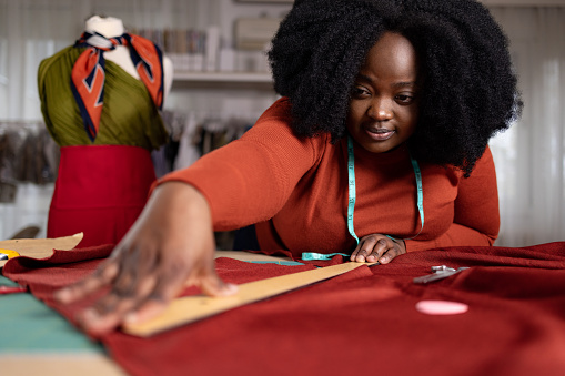 African American female designer measuring textile with a ruler while working in a clothing design studio.