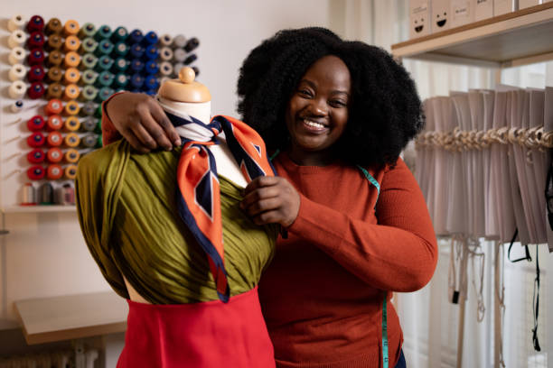 Happy African American female tailor working on mannequin in clothing studio. Happy black female designer working on a mannequin in a clothing studio and looking at camera. fashion designer stock pictures, royalty-free photos & images