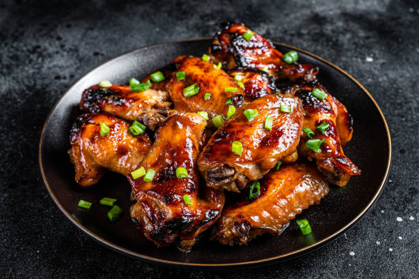 asas de frango assadas com molho de pimenta doce em um prato. fundo preto. vista superior - wing chicken barbecue grilled - fotografias e filmes do acervo