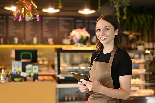 Smiling caucasian woman coffee shop owner using digital tablet to receiving online orders.