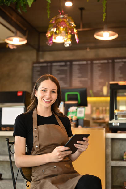 istock Image of successful small business owner using digital tablet and looking at camera while sitting in her modern coffee shop. 1451324442
