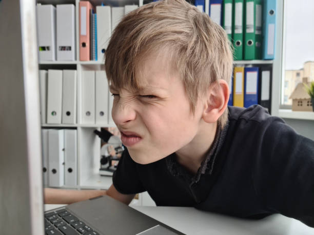 istock Teenager boy squints using a laptop with poor eyesight sits and looks at computer 1451325594