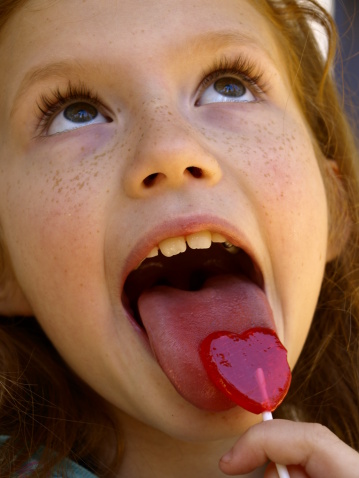 Young girl licking a heart shaped lollipop.  