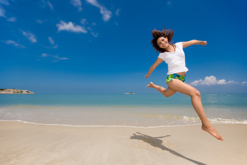 young beautiful girl jumping happily at the beach feeling free and emancipated