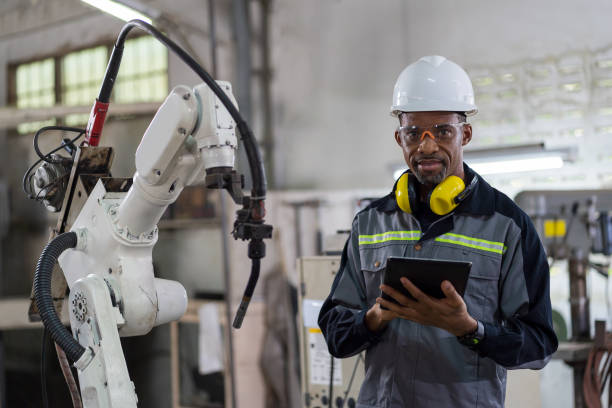 istock African American male engineer worker holding digital tablet working with welding robot arm in workshop. Male worker control automatic welding robot arm in factory 1451343662