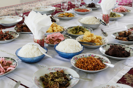 Various food buffet served on floor dining style with bokeh background. Masakan Padang, Indonesian culture traditional cuisine. Often in Ramadan month and Islam Eid Al Fitr and Al Adha celebration.