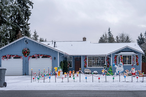 American house with snowy yard decorated for New Year and Christmas by figurines of Santa Claus, deer, snowman, bigfoot, christmas tree, garlands. Everett, WA, USA - December 2022