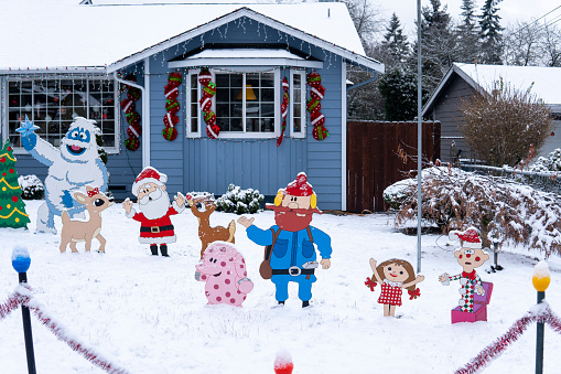Snowy yard of the house is decorated with New Year and Christmas figurines of Santa Claus, deer, bigfoot, christmas tree. Everett, WA, USA - December 2022