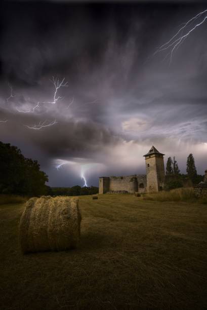 A vertical shot of the tower and field with a hay roll during a thunderstorm.