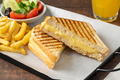 Cheddar cheese toast with french fries and salad on wooden table