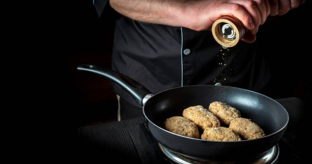 istock Cooking meat cutlets on grill pan by chef hands on black background for copy space text restaurant menu. The chef adds pepper 1451360324