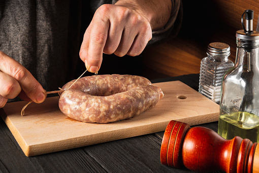 Close-up hands of a cook tying a thread of homemade sausage. Cooking sausages with meat and spices on a cutting board