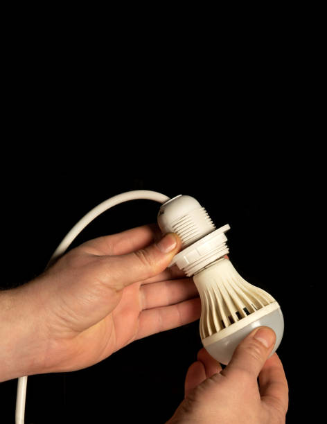 close-up de mãos de um eletricista instalando uma lâmpada elétrica que economiza energia - lighting equipment illuminated isolated on black part of - fotografias e filmes do acervo