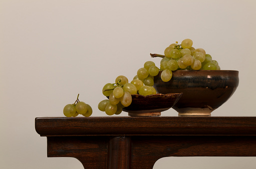 White grapes on Chinese antique plate on wooden table against white wall