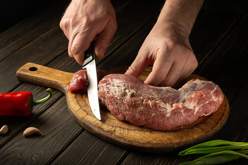 Close-up of a chef hands cutting raw veal meat on a cutting board before cooking. Peasant foods