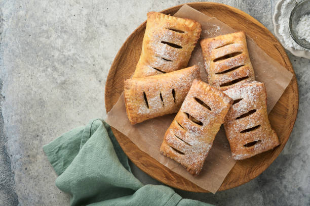 handkuchen. mini-blätterteig oder handpasteten mit apfel gefüllt und zuckerpulver in holzteller streuen. hausgemachter kuchensnack mit kruste zum frühstück rustikales foto.  speicherplatz kopieren. - pie apple apple pie dessert stock-fotos und bilder