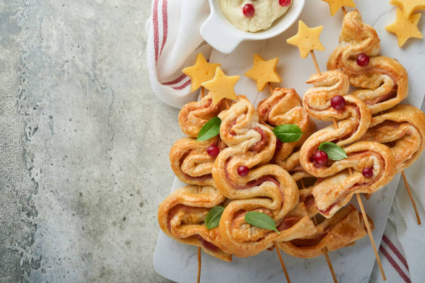 istock Christmas or New Year appetizer. Christmas tree shape puff pastry buns with cheese and ham. Group of Christmas tree shapes on marble stand. Festive idea for Christmas or New Year dinner. Top view. 1451371583
