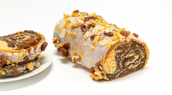 Isolated Christmas strudel Makowiec with poppy seeds, traditional polish festive cake covered with sugar icing, walnuts, dried fruits on white background. Horizontal plane