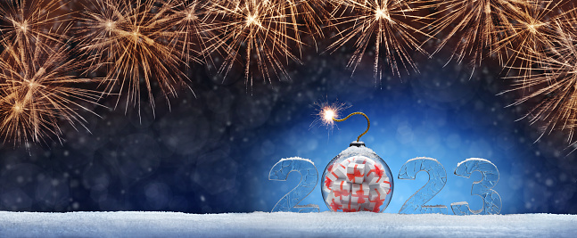 New Year card with ice number 2023 on snow. Christmas tree toy of a ball with gifts in the form of a bomb. Festive banner with salutes against the background of night abstract defocused light