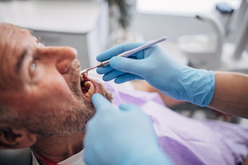 Male dentist working on mature male patient's teeth in dentist's office.
