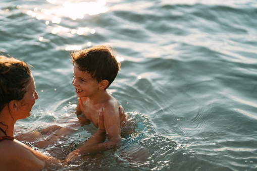 Photo of a little boy and his mother taking a moment for themselves  and ending busy week on a local beach, bathing in the sea