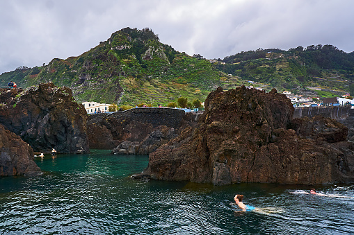 Porto Moniz, Portugal - November 22, 2022: People swim in the natural pools in the rocks at Porto Moniz in Madeira in winter.